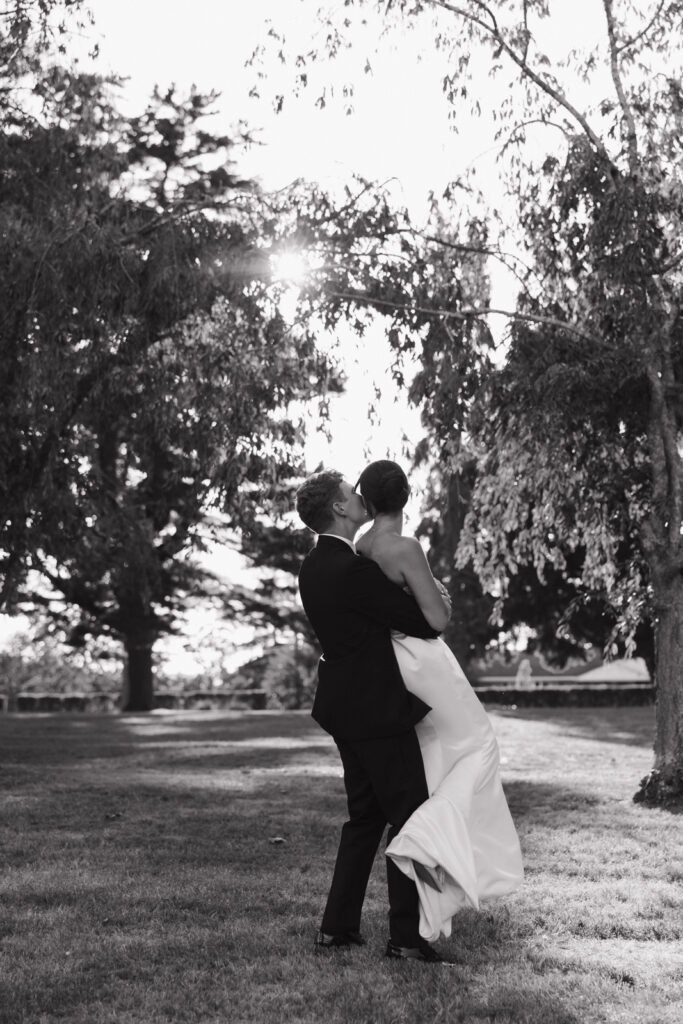 Black-and-white documentary wedding photography capturing the bride and groom twirling around under trees. 