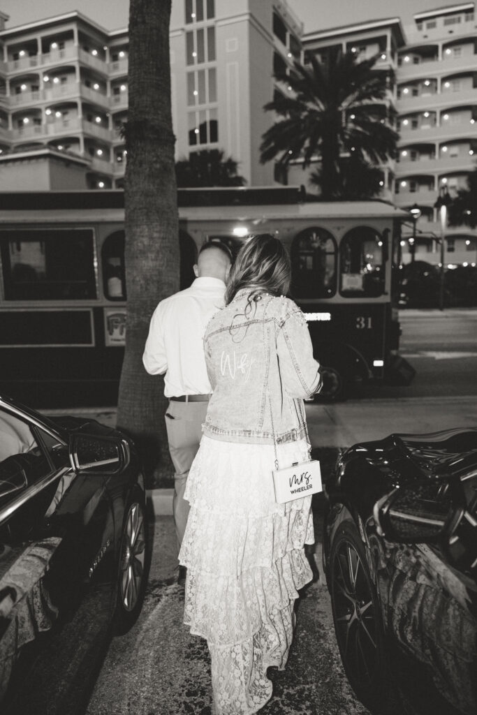 Black-and-white documentary-style wedding photo of the bride and groom walking to their wedding rehearsal dinner. 