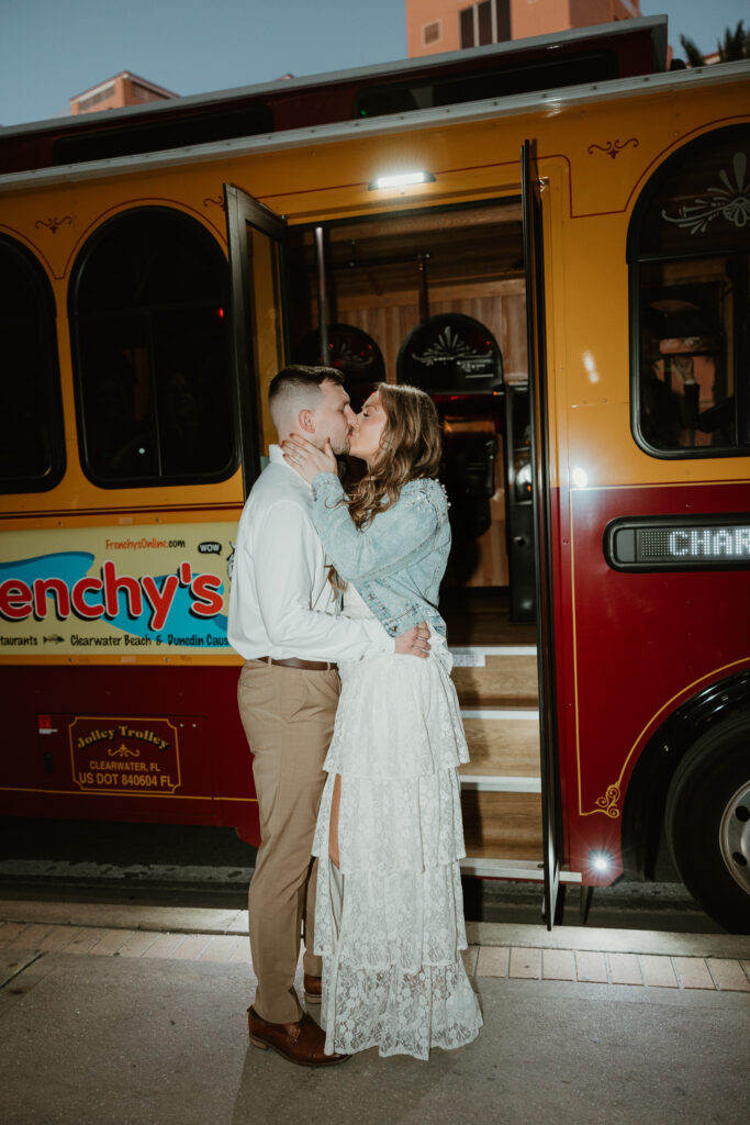 The soon-to-be bride and groom are kissing in front of a trolley bus on their way to their wedding rehearsal dinner on a cruise. 