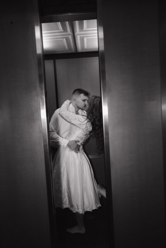 Black and white editorial wedding photography of the bride and groom kissing in a hotel elevator. 