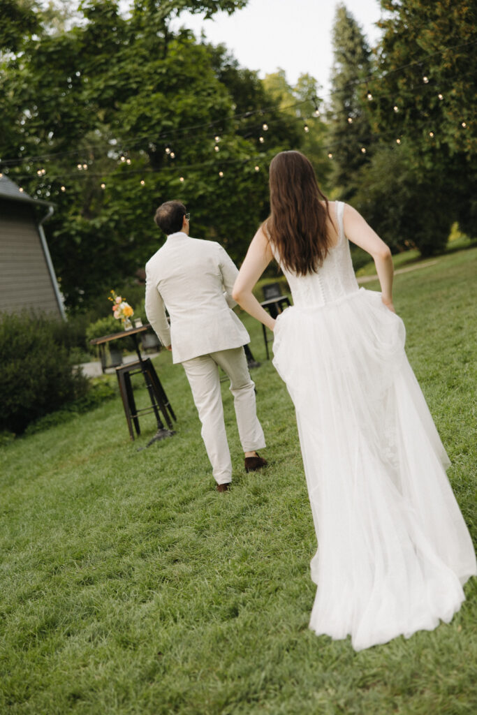 A bride and groom walking into the cocktail hour of their Hudson Valley, New York, summer wedding. String lights through the trees create an intimate wedding in upstate New York, captured by a documentary-style wedding photographer.  