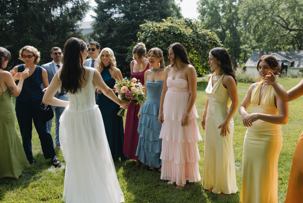 A bride in a vintage lace white dress gives an intimate first look to her bridesmaids. Pastel hue bridesmaid dresses. Hudson Valley, New York, intimate summer wedding. 