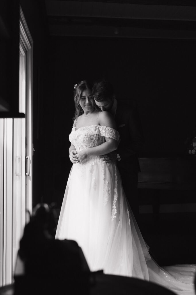Black and white documentary style wedding photography. The groom stands behind the bride, hugging her at their Connecticut luxury wedding.
