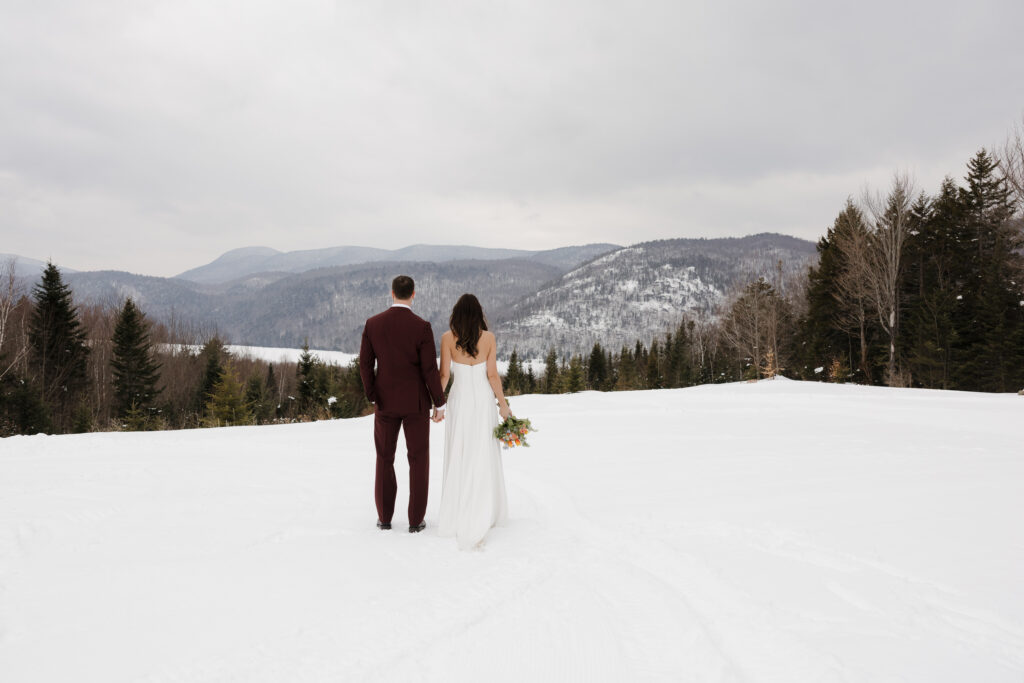 The bride and groom stand side-by-side looking out to the Adirondack winter mountain range. Outdoor  Adirondack winter wedding.