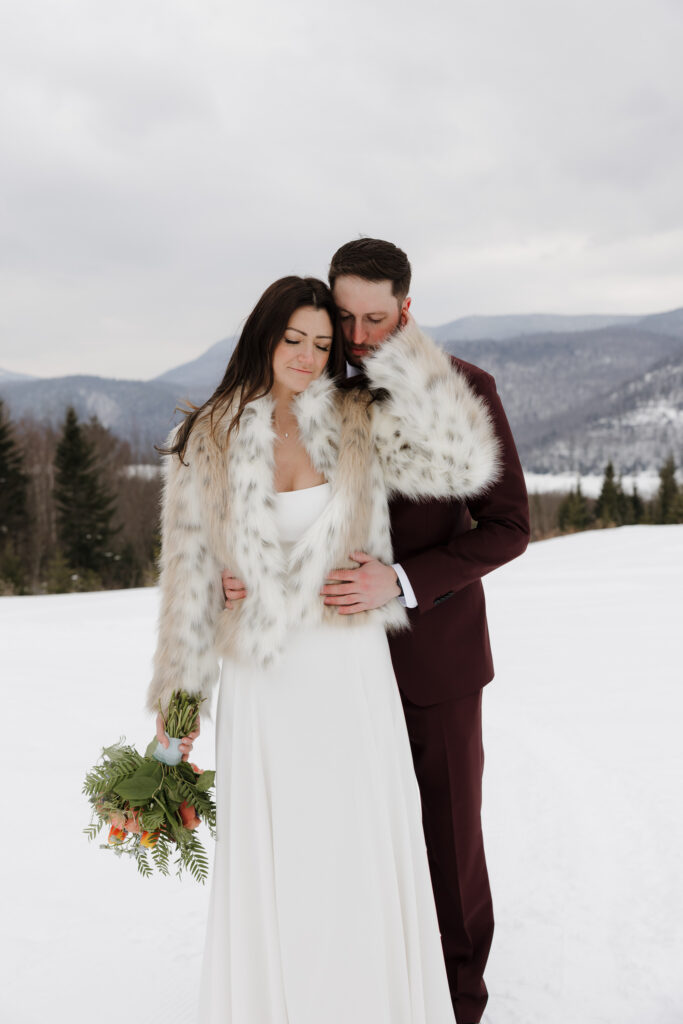 Bride and groom standing next to each other after their dreamy winter wedding outside in the Adirondack Mountains. 