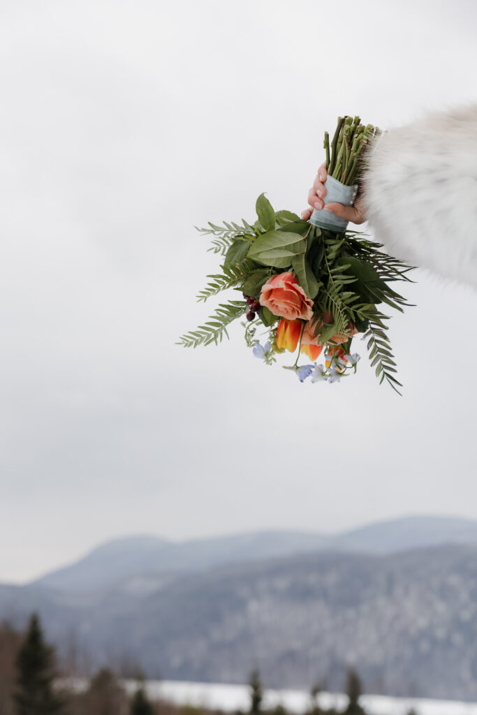 Beautiful ferns, pink roses, and lilac flowers of the bridal bouquet, the bride holds the bouquet with fresh snow on the ground.