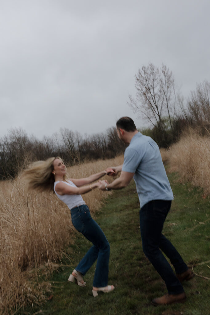 Playful couple spinning together in an open field during a couples photography session.
