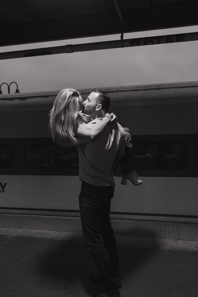 Couple kissing in front of a train as it goes by on the train station platform 