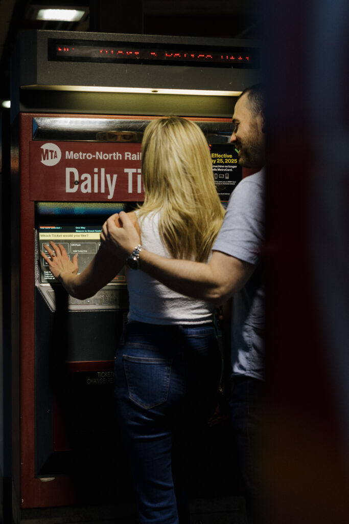 Candid photo of a couple at a Metro-North ticket machine during a playful engagement session.