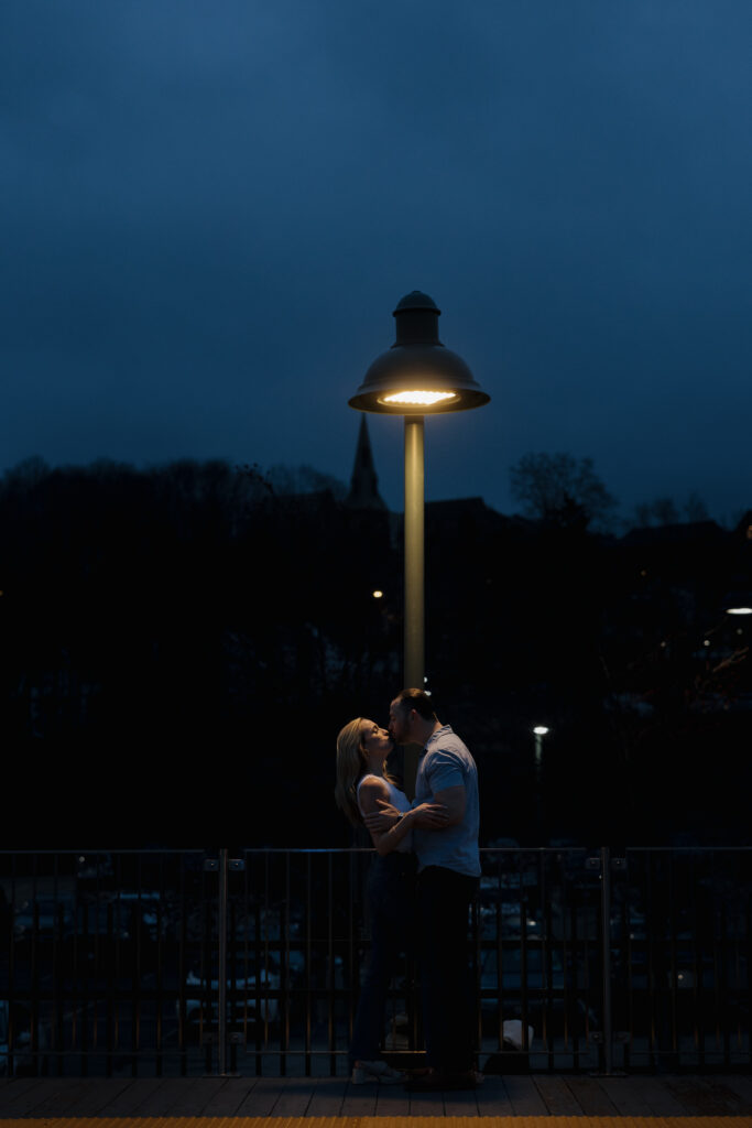 Couple kissing under a glowing streetlamp at night during a Connecticut engagement session.