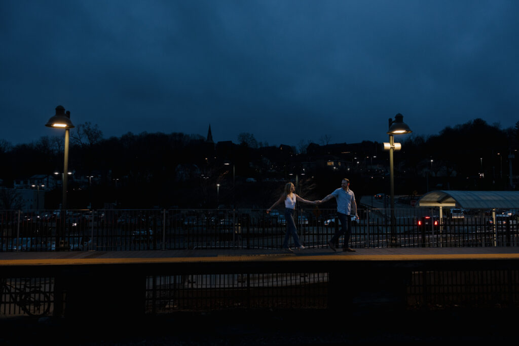 Couple holding hands and walking across a train platform at dusk during a CT engagement session.