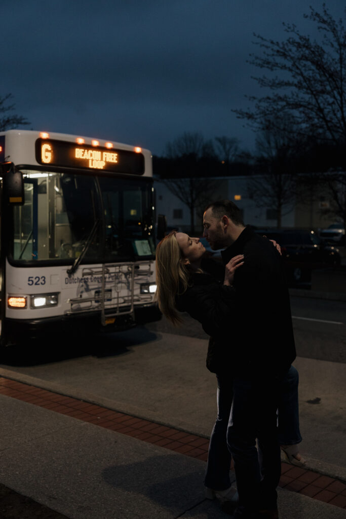 Couple kissing in front of a bus at night during a Connecticut engagement session with a city feel.