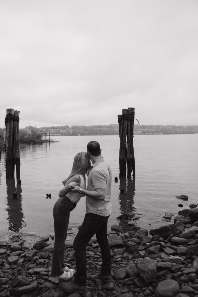 Black and white photo of a couple standing by the water during a quiet engagement session.