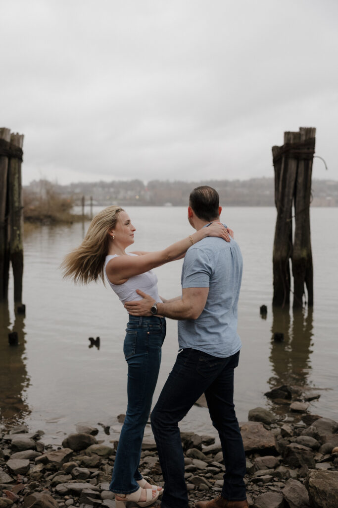 Couple dancing together on a rocky shoreline during an engagement session by the water.