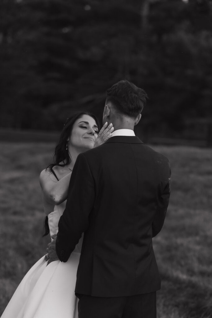 Black and white photo of bride leaning in close to groom's face smiling tenderly during wedding portraits