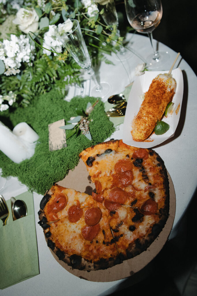 Wedding reception late night snack of pepperoni pizza on a table beside white floral centerpiece and champagne glass