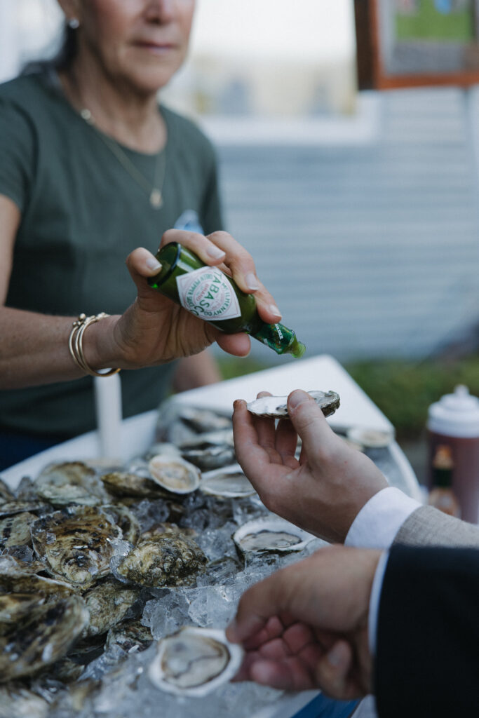 Guest receiving a freshly shucked oyster with hot sauce at an outdoor wedding cocktail hour oyster station