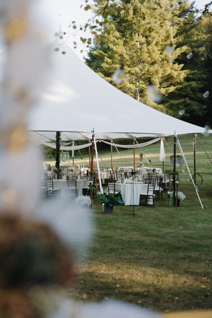 Elegant outdoor tented wedding reception with white draped sailcloth tent, chiavari chairs, and white floral centerpieces on a lush green lawn